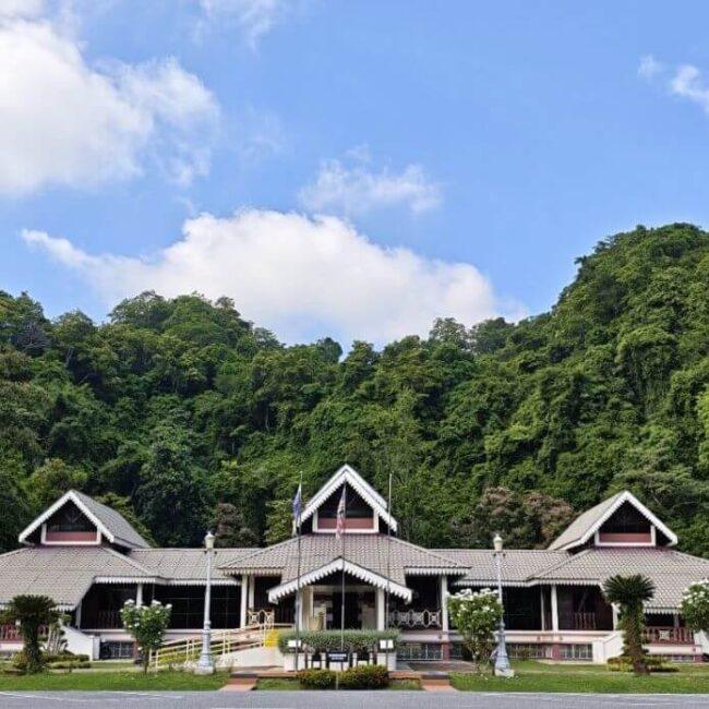 Traditional building with three gabled roofs set against a lush green hillside under a blue sky
